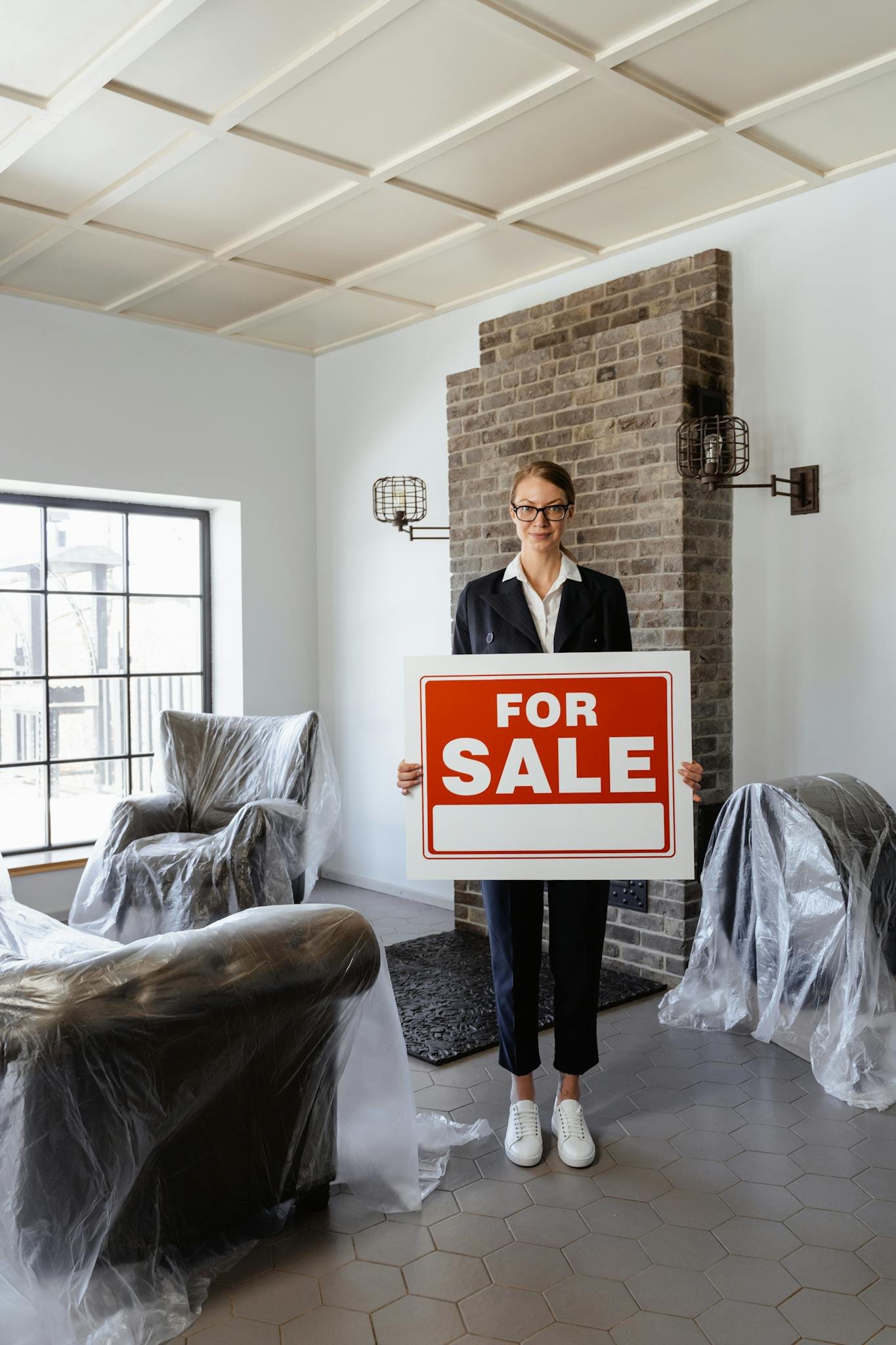 Professional real estate agent holding a 'For Sale' sign in a furnished indoor setting.